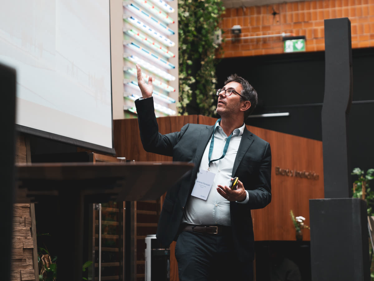A speaker on stage gesturing towards a presentation screen