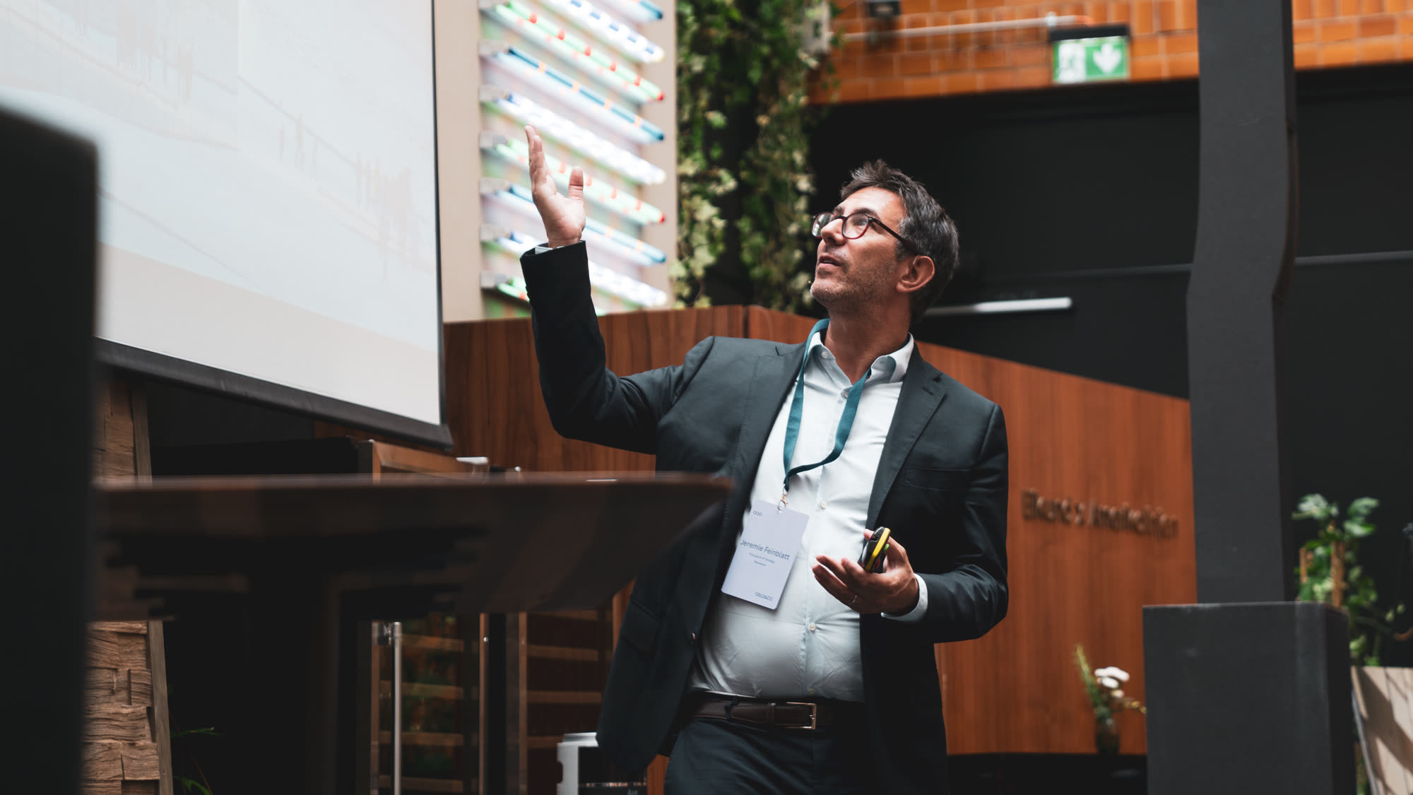 A speaker on stage gesturing towards a presentation screen